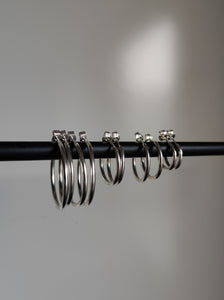 A group of Kathrin Jona silver hoop earrings in different sizes hanging on a metal rod.