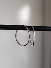 Load image into Gallery viewer, A pair of Kathrin Jona silver round hoop hinge earrings hanging on a black rod.
