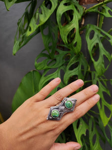 A hand holding a Green Shield Turquoise Ring #1 with a green stone by Kathrin Jona.