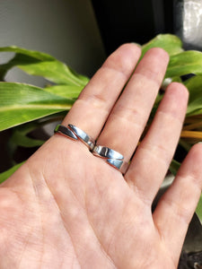 A hand holding two Kathrin Jona Mother of Pearl Granulation Rings in front of a plant.