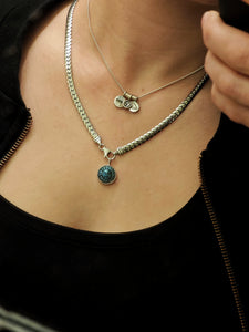 A person wearing a sterling silver chain necklace with a round turquoise pendant and an elegant silver necklace adorned with Kathrin Jona Charm Spacers, exuding charm and sophistication.