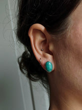 Load image into Gallery viewer, Close-up of a person&#39;s ear adorned with two earrings: a small sterling silver hoop in the helix and an Oval Turquoise Stud by Kathrin Jona in the lobe.
