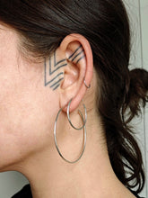 Load image into Gallery viewer, A close-up showcases a person&#39;s ear embellished with geometric line tattoos and two Thin hoops earrings, studs by Kathrin Jona. The individual sports dark hair neatly tied back, accentuating the intricate design.
