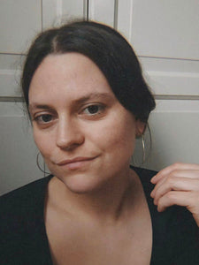 A person with dark hair, adorned in Kathrin Jona's thin hoop earrings, gazes at the camera with a neutral expression against a light-colored background.