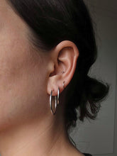 Load image into Gallery viewer, A person with dark hair presents a selection of Kathrin Jona earrings, featuring Hoops - different sizes and a small stud, all made from recycled 925 sterling silver on their left ear. The neutral background accentuates the elegant simplicity of the jewelry.
