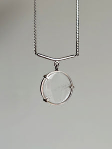 The Clear Quartz Moto Necklace by Kathrin Jona features a round, Clear Quartz pendant gracefully hanging from an upcycled silver chain against a simple background.