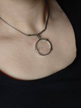 Load image into Gallery viewer, A person wearing the Clear Quartz Moto Necklace by Kathrin Jona, featuring a circular pendant made from recycled 950 sterling silver, over a black shirt.
