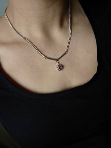 Close-up of a person wearing the Kathrin Jona Amethyst Moto Bar Necklace, which features a heart-shaped purple amethyst pendant, against a dark shirt.