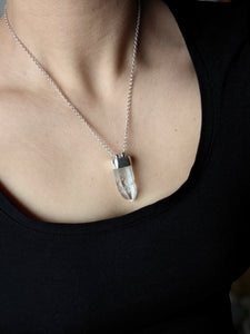 A person wearing a black shirt and the Australian Clear Quartz Necklace #2 from Kathrin Jona, featuring a clear quartz pendant on an adjustable silver chain.