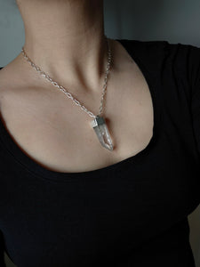 A person is adorned with a Kathrin Jona Australian Clear Quartz Necklace #1, featuring a silver chain and a large, clear quartz pendant.