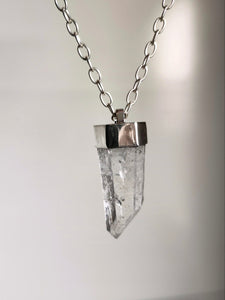 The Australian Clear Quartz Necklace #1 by Kathrin Jona features a stunning clear quartz crystal pendant with a silver cap, elegantly hanging from an Australian silver chain, set against a neutral background.