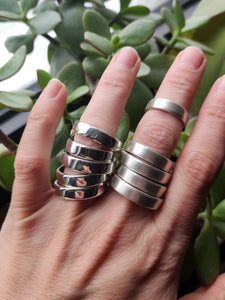 A woman's hand holding a set of wide band silver Stacker rings by Kathrin Jona.