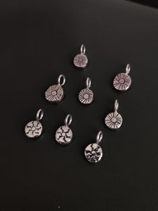 A group of small Kathrin Jona sterling silver charms on a black surface, including a 'SUN' charm.