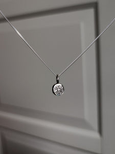 A Kathrin Jona sterling silver necklace, adorned with a 'SUN' charm, hangs from a door.