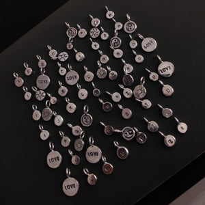 A group of Kathrin Jona 'INITIAL' silver letter charms, arranged on a table.
