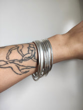 Load image into Gallery viewer, A woman wearing Round Silver Bangles hand forged from 925 sterling silver, with tattoos on her arm.
