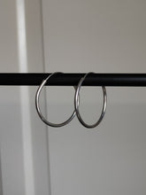 Load image into Gallery viewer, A pair of Kathrin Jona silver round hoop hinge earrings hanging from a metal rod.
