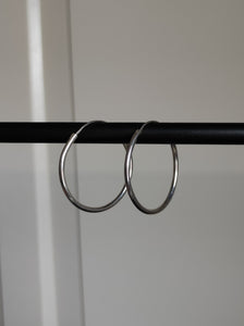 A pair of Kathrin Jona silver round hoop hinge earrings hanging from a metal rod.