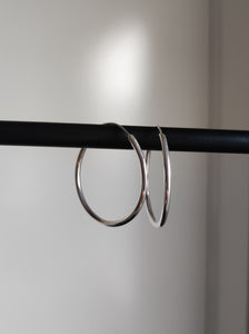 A pair of Kathrin Jona silver round hoop hinge earrings hanging on a black rod.