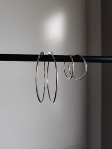 A pair of Kathrin Jona thin hoop earrings hanging on a rod.