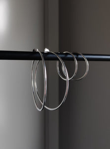 A pair of Kathrin Jona thin hoop earrings hanging on a rod.