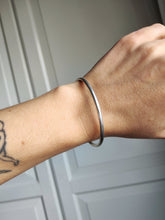 Load image into Gallery viewer, A woman wearing a Round Silver Bangle by Kathrin Jona with a tattoo on it.
