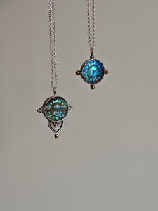 Two Kathrin Jona Fair Labradorite Sun Face Necklaces, crafted from recycled silver with round pendants showcasing blue and green sun designs, hanging against a plain background.