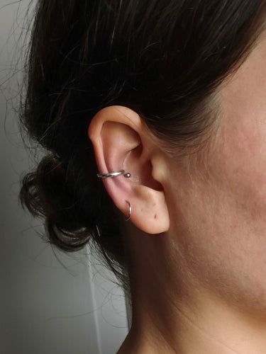 A person with curly hair showcases two hoop piercings, complemented by the sleek 