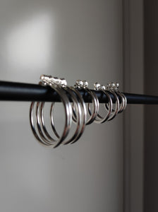 Four Kathrin Jona silver hoop earrings of different sizes hanging on a black rod.