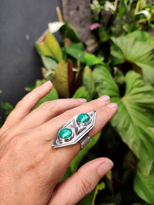 A hand holding a Green Shield Malachite Ring #3 from Kathrin Jona in front of plants.