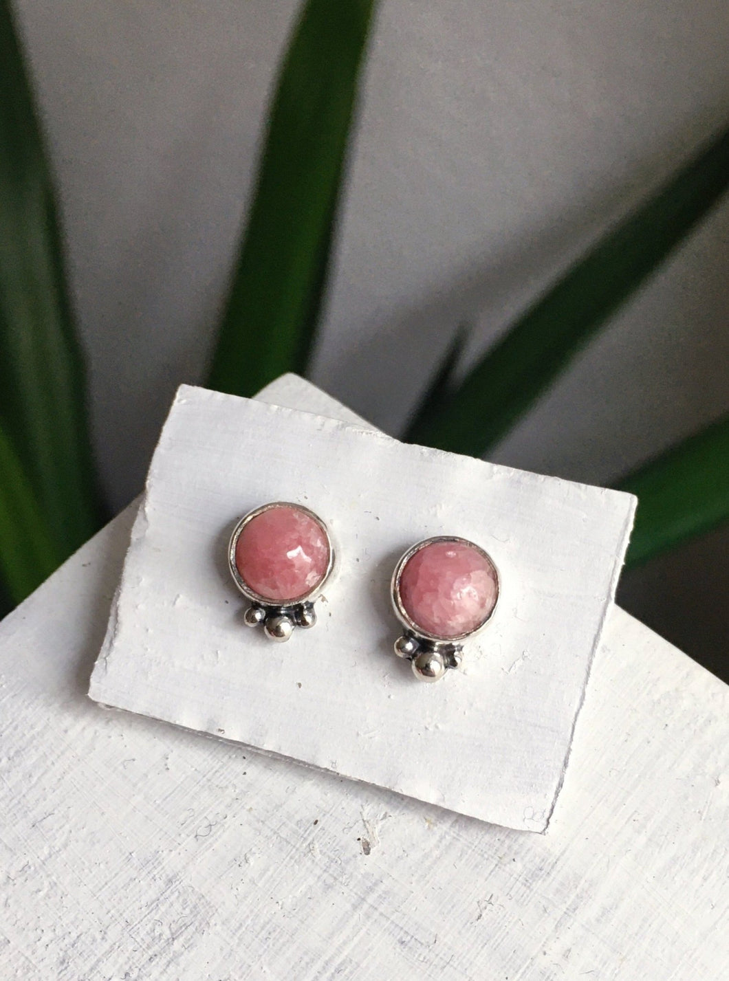 A pair of Rhodochrosite Studs by Kathrin Jona on a white table.