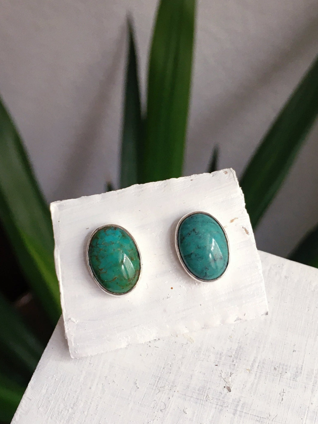 A pair of Oval Turquoise Studs by Kathrin Jona sitting on top of a wooden box.