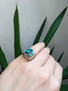 A hand holding a Kathrin Jona Turquoise Cluster Signet Ring.