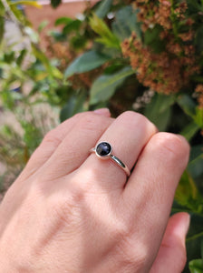 A hand holding a Round Obsidan Silver Stacker Ring with a black sapphire stone by Kathrin Jona.