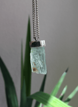 Load image into Gallery viewer, A piece of Aquamarine Necklace No.4 by Kathrin Jona on a silver chain hanging from a plant.
