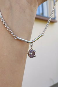 A woman is holding a Kathrin Jona silver Amethyst Moto Bar Necklace.