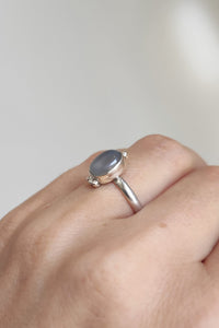 A woman's hand holding a Kathrin Jona Chalcedony Stacker Ring with a blue stone.