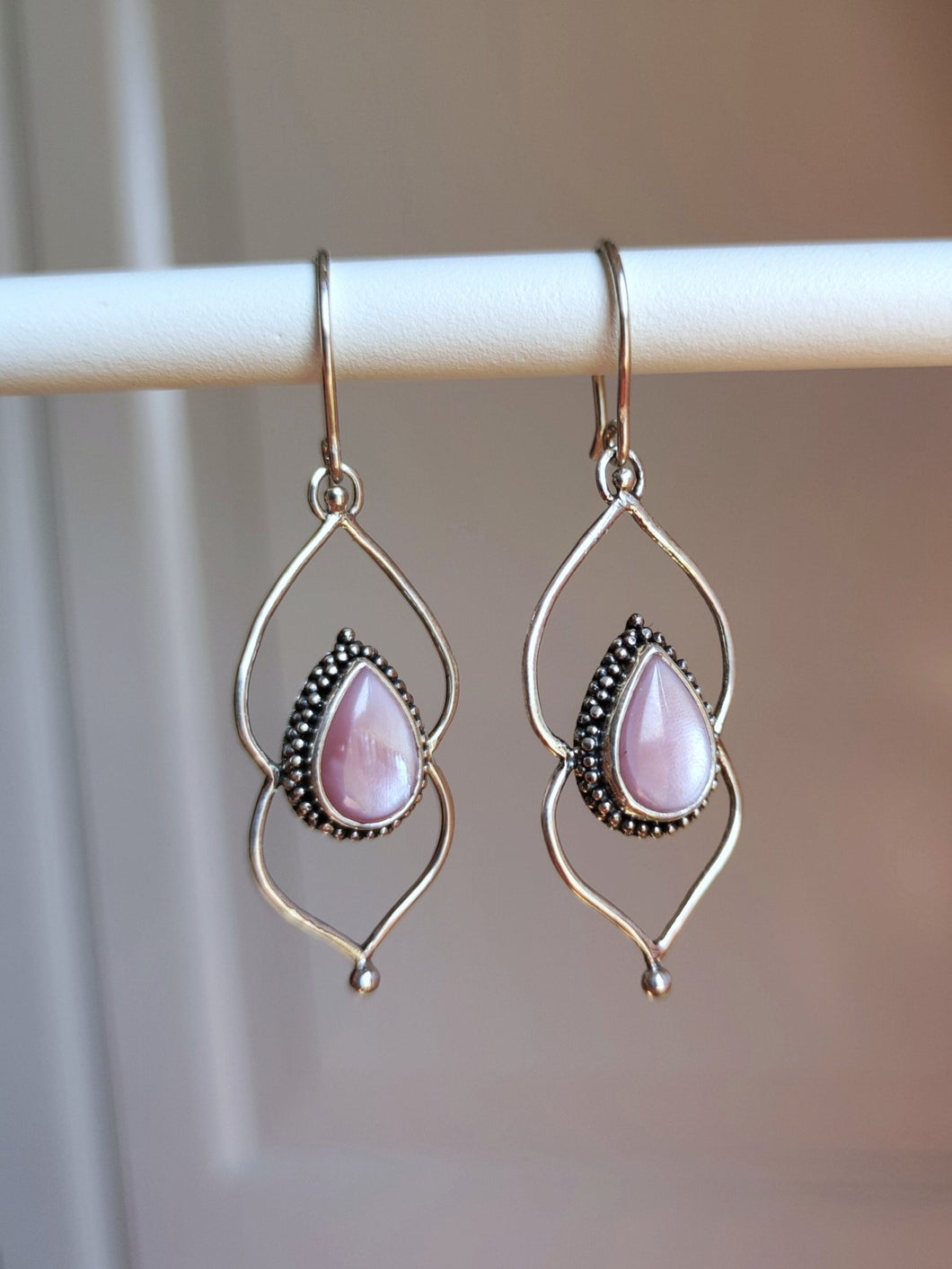 A pair of Kathrin Jona Pink Mother of Pearl Drop Granulation Earrings hanging on a hanger.