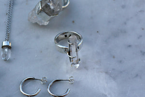 A Kathrin Jona clear quartz double point ring, earring, and necklace on a marble table.