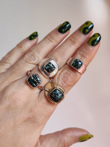 A woman's hand holding a Kathrin Jona Leopard Opal Silver Ring M with a green and black stone.