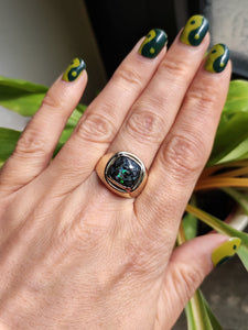 A hand holding a Leopard Opal 9k Gold Signet Ring with a green and black stone by Kathrin Jona.